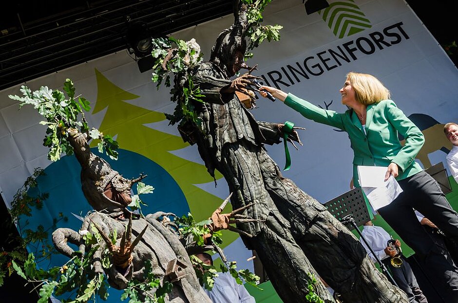 EdWood - Ein Mensch als Baum verkleidet steht auf der Bühne mit anderen Teilnehmern des Waldgipfels.